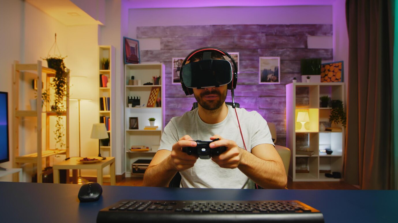  A gamer sits at a desk, focused on playing, with a game controller in hand and wearing a headset, in a stylish, colorful room.