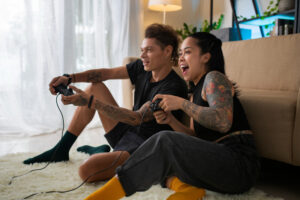 A couple sitting on a plush rug in a cozy, well-lit living room, focused on playing video games together.