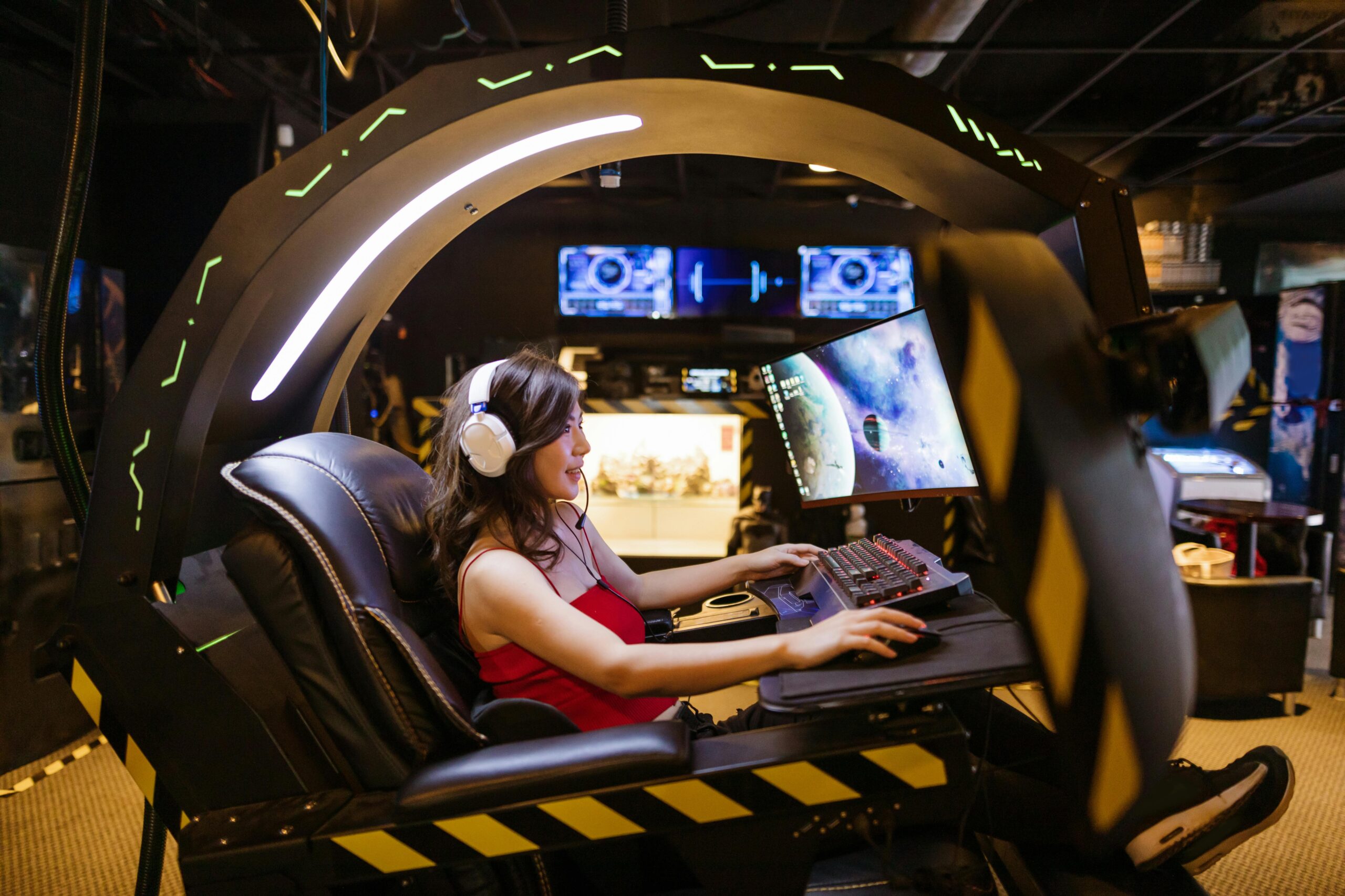 A gamer sits in a high-tech gaming chair, focused on a screen displaying a colorful space scene, surrounded by a futuristic environment.