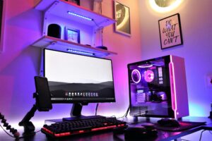 A vibrant gaming setup featuring a monitor, mechanical keyboard, and a RGB-lit PC case, against a stylish backdrop with artwork.