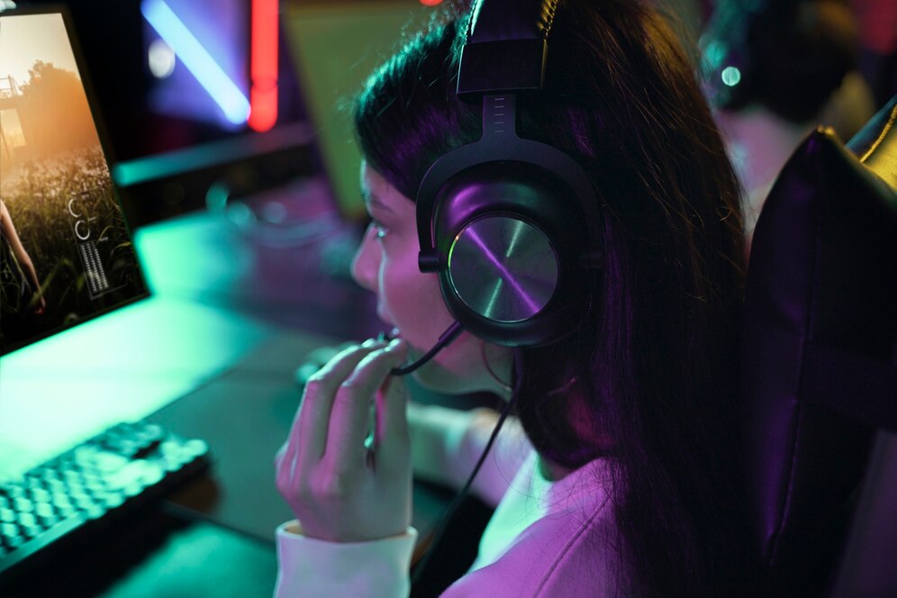  A person wearing headphones, seated at a gaming setup, engaged with a colorful screen and illuminated keyboard.