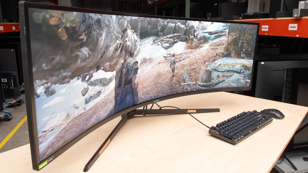  A curved gaming monitor displays a vibrant scene from a video game, accompanied by a keyboard and mouse on a wooden desk.