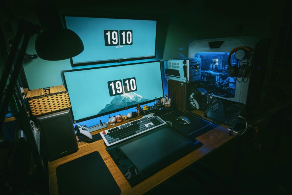 A modern workspace featuring dual monitors, a mechanical keyboard, tablet, gaming console, and a illuminated PC tower.