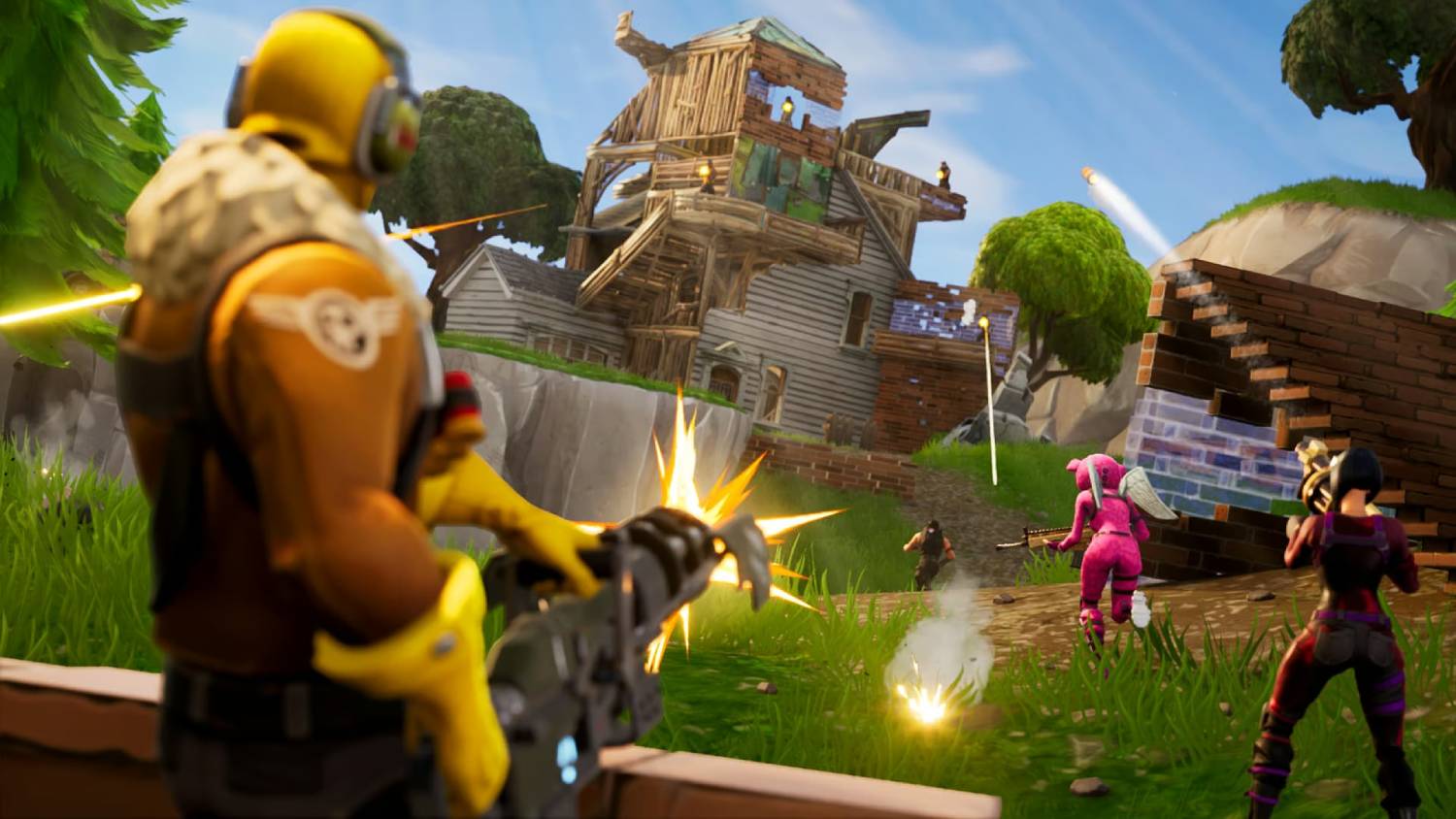 A battle scene from a video game featuring colorful characters shooting weapons at a partially destroyed wooden house on a grassy battlefield.