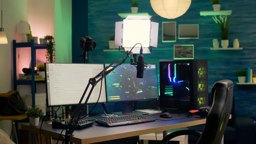 A modern gaming setup featuring dual monitors, a microphone on an arm, gaming keyboard, and colorful PC case in a stylish room.
