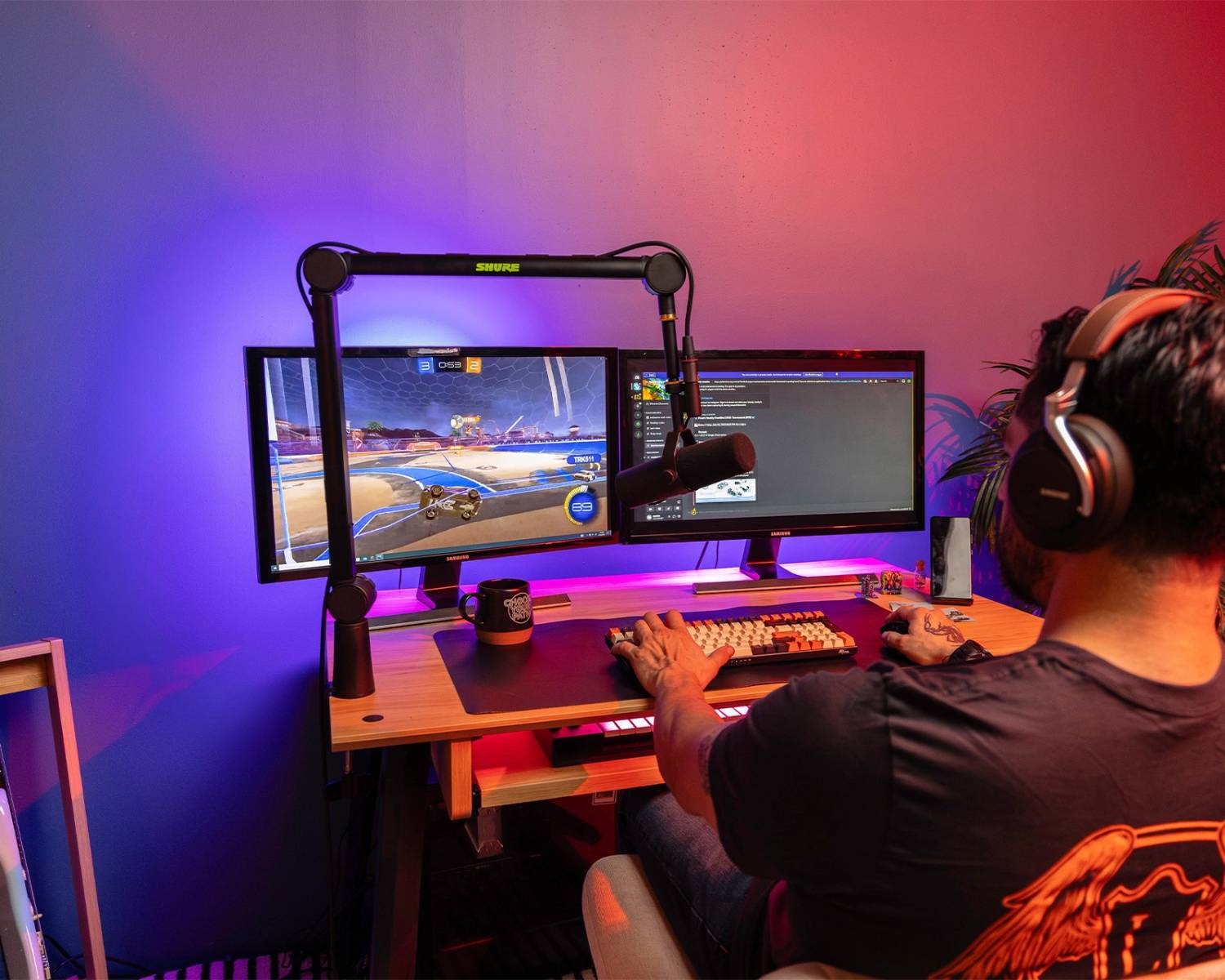 A gamer using two monitors to play Rocket League, with colorful LED lights, a microphone, and a keyboard, outfitted for streaming.