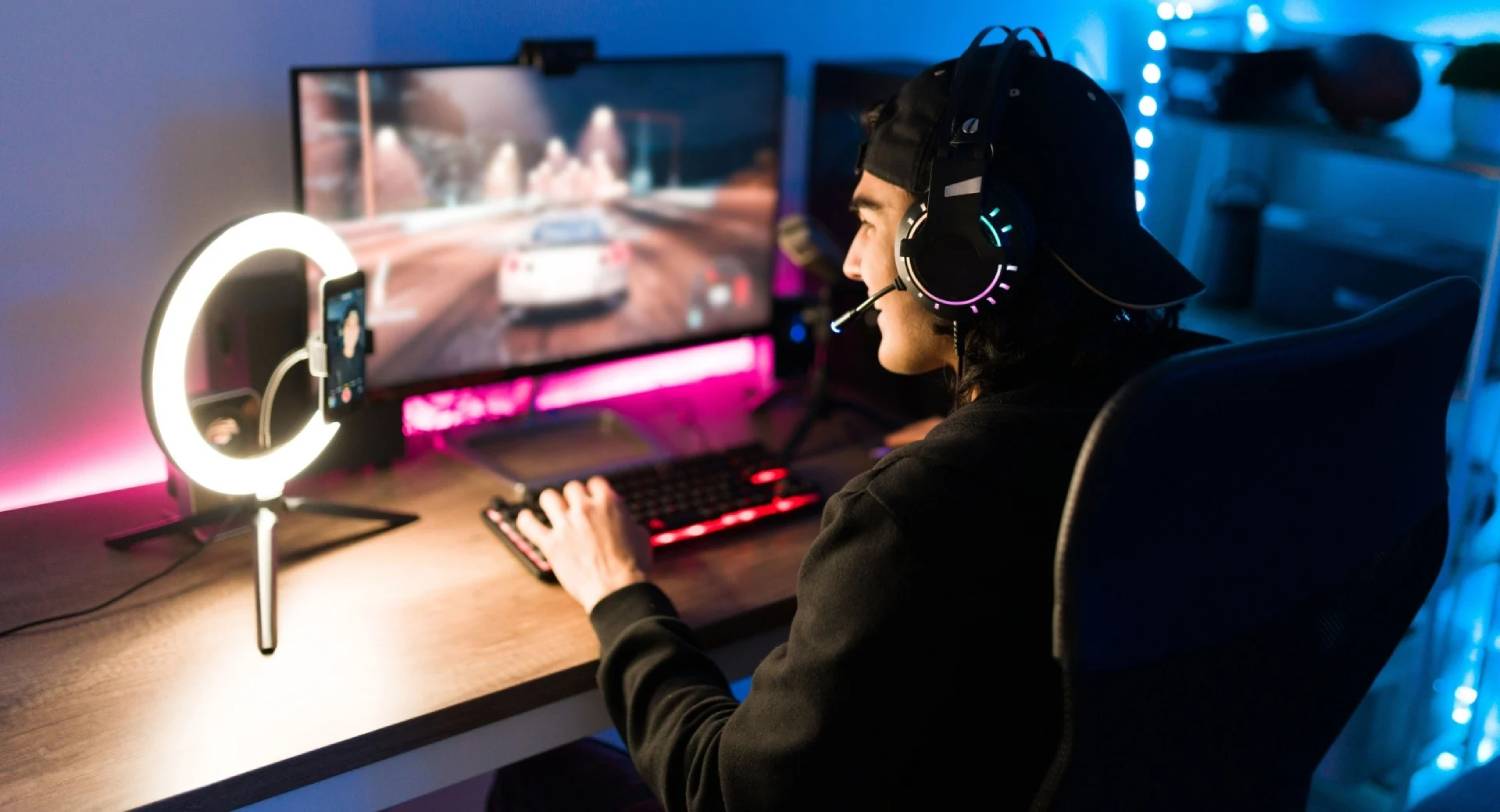 A gamer in a dark room focuses on an action-packed racing game displayed on a monitor, with vibrant LED lights illuminating the setup.