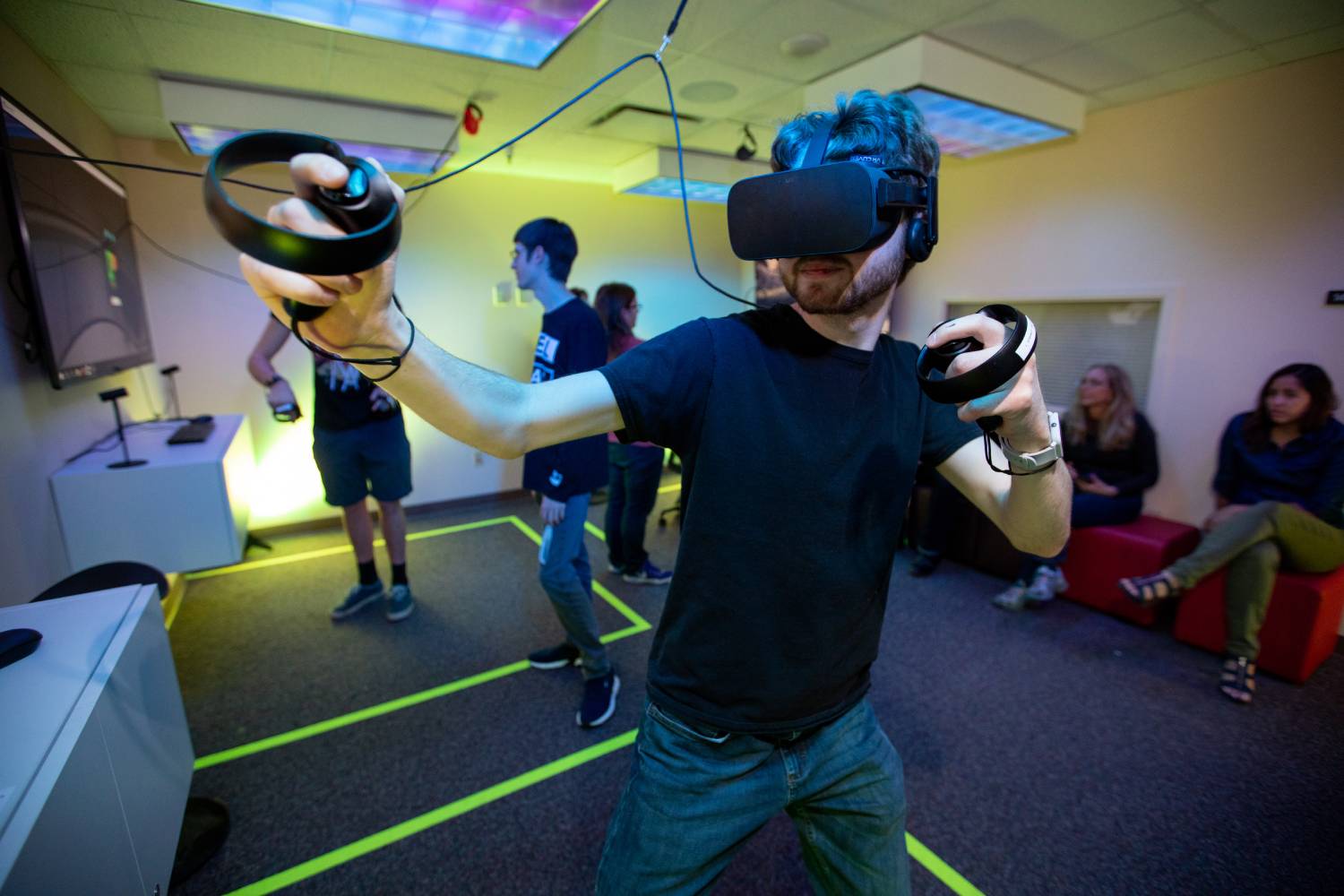 A person wearing a VR headset engages in an immersive experience, surrounded by others enjoying virtual reality in a vibrant room.