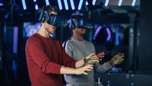 Two individuals wear VR headsets in a modern gaming space, engaging with virtual objects illuminated by colorful neon lights.