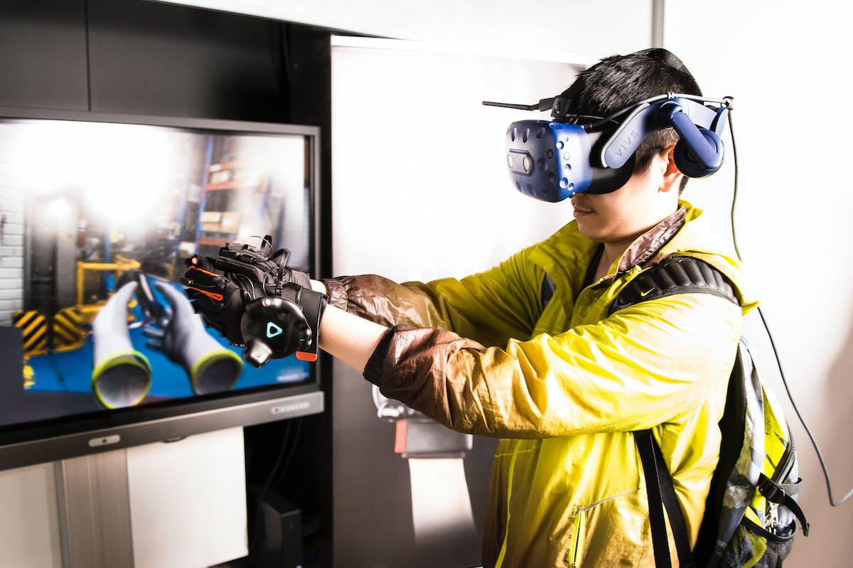 A person wearing a virtual reality headset and motion gloves interacts with a VR display showcasing an industrial setting.