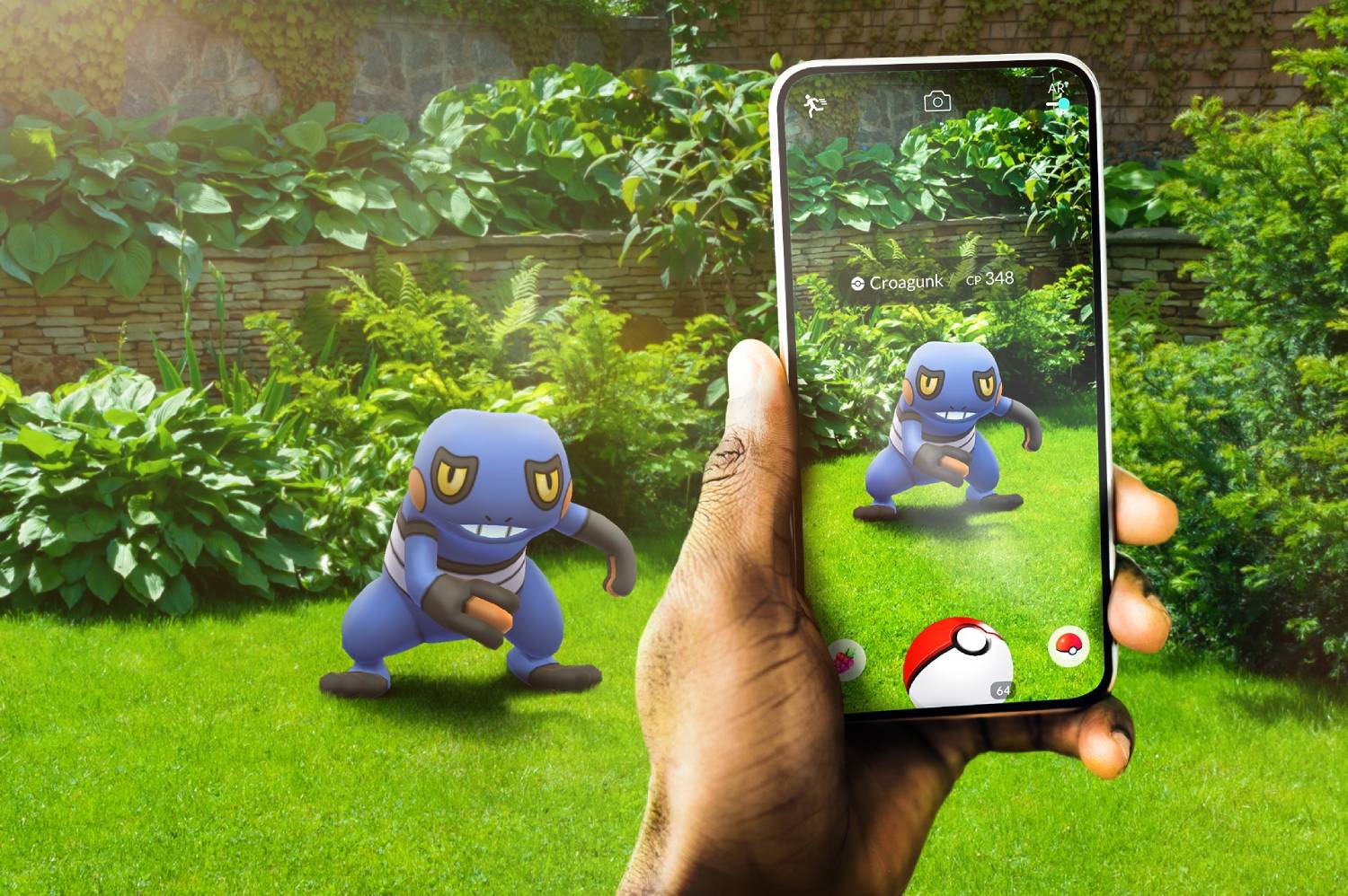 A hand holds a smartphone displaying a Croagunk in augmented reality, set against a lush garden backdrop.