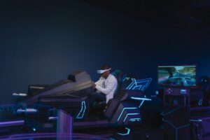 A person sits in a futuristic racing simulator with blue neon lights, focused on a screen displaying a racing scene.