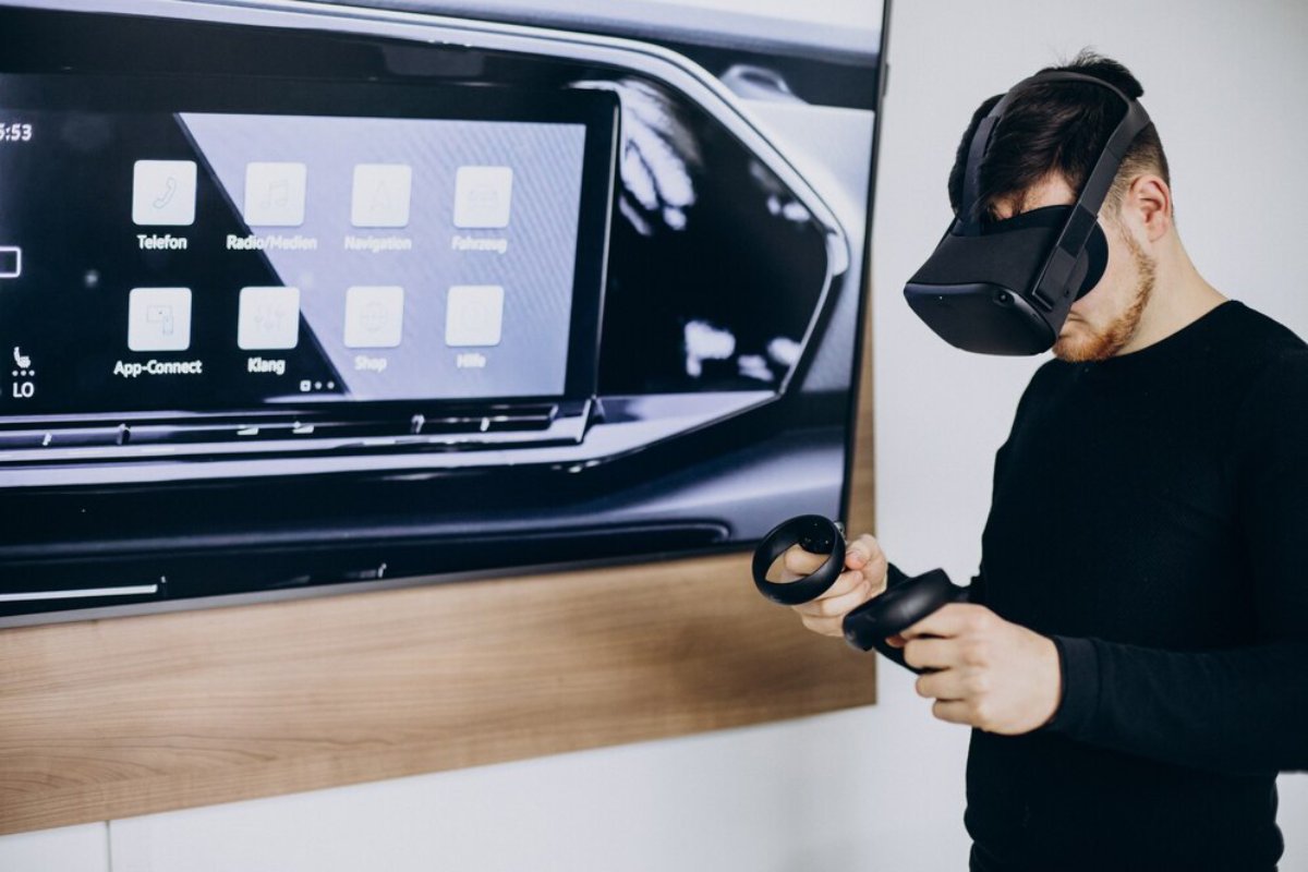 Man using virtual reality headset and controller near a screen displaying car dashboard interface.