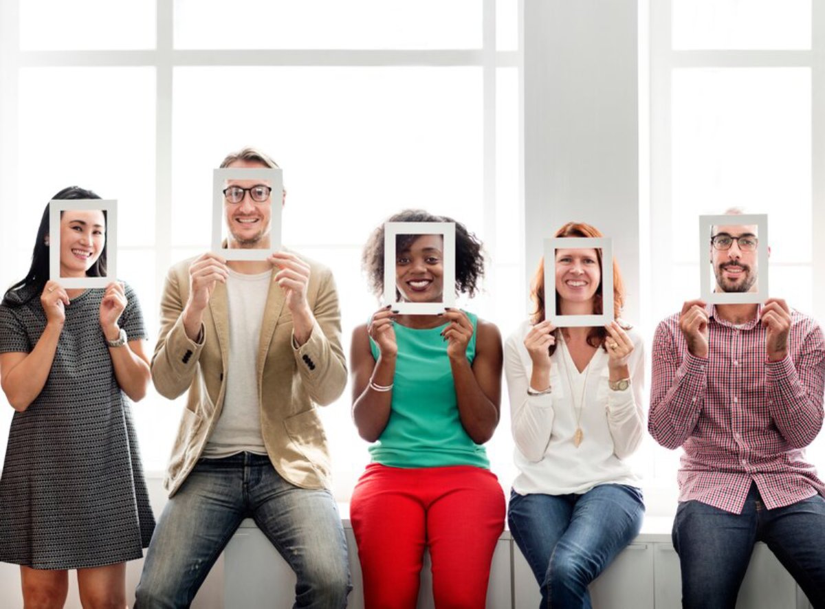 Five people holding frames in front of their faces, sitting by a window with bright sunlight.