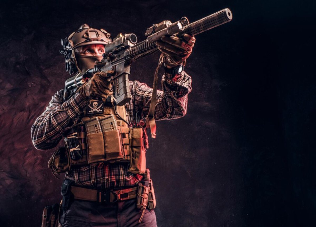 A soldier in tactical gear aiming a rifle upwards, surrounded by a smokey, dark background.