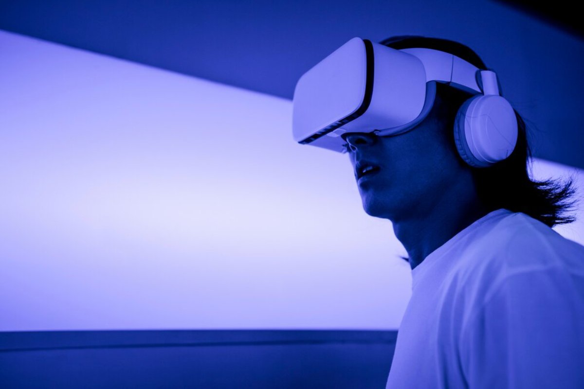 Person wearing a virtual reality headset and headphones in a room illuminated by blue light.