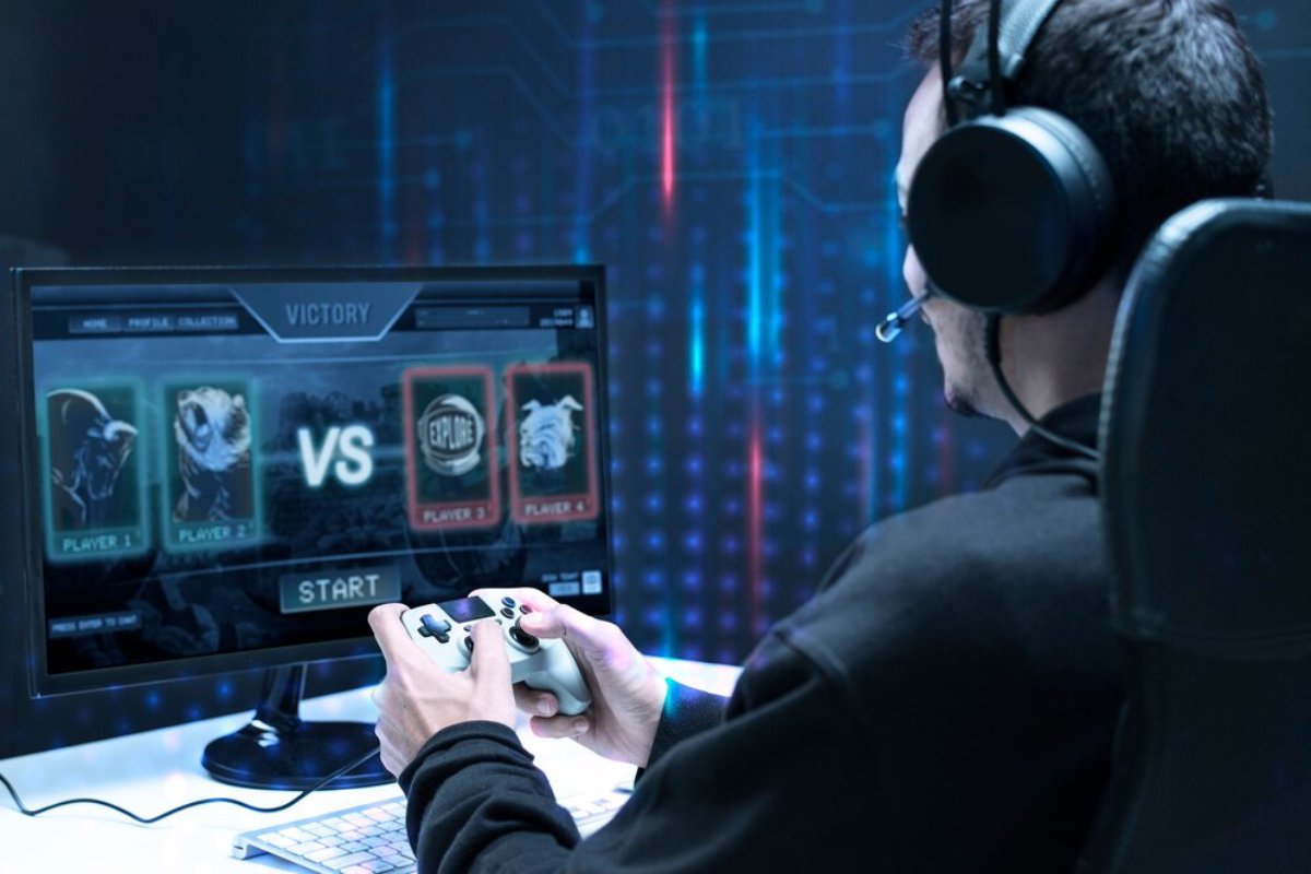 Man in headphones playing a video game with a controller, looking at a computer screen displaying a game victory screen.