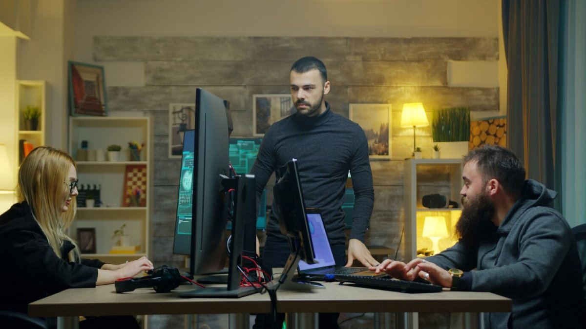 Three colleagues in a modern office work on computers, discussing a project.