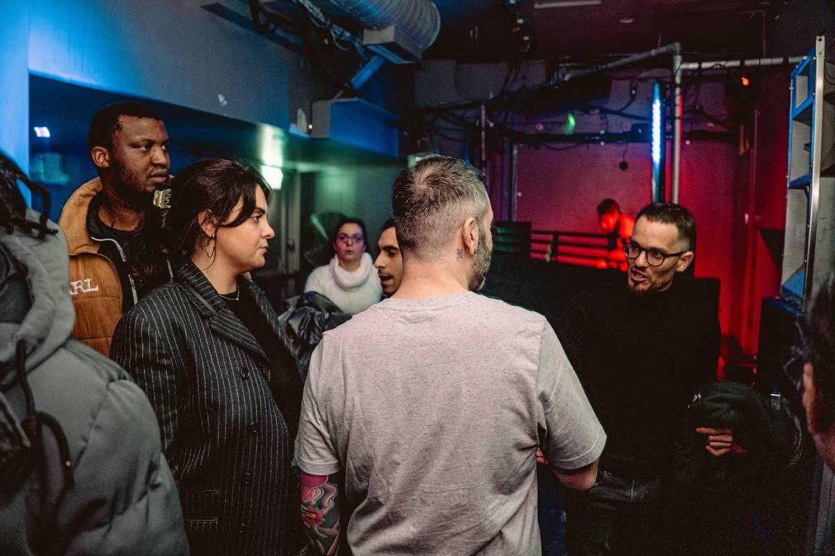 A group of diverse people engaged in a serious conversation in a dimly lit club setting.