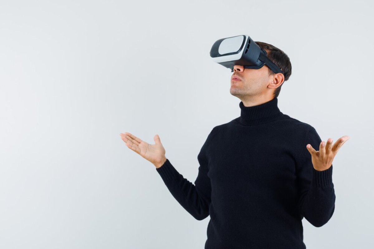 Man in black turtleneck using virtual reality headset, gesturing with hands raised.