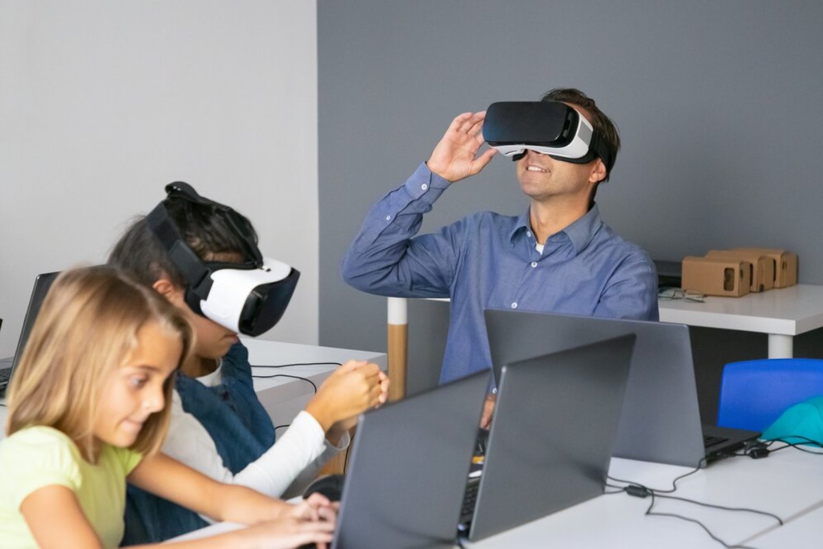 A man and two children using virtual reality headsets in a modern classroom.
