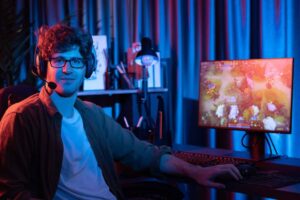Young man gaming at a computer desk with neon lighting, wearing headphones and a microphone.