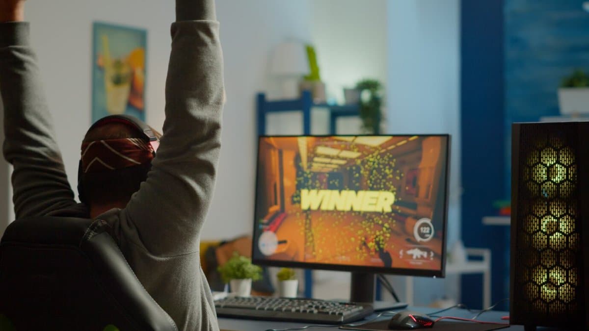 Person in headphones celebrating a win on a computer game screen in a cozy, well-lit room.